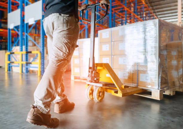 Warehouse worker is working with hand pallet truck and cargo pallet