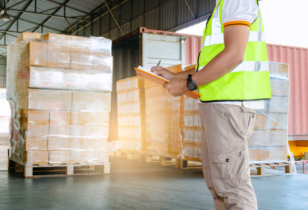 Warehouse courier shipment transportation. Warehouse worker is inspecting load control the shipment, stacked cardboard boxes on pallet and truck docking at warehouse loading bay stock pictures, royalty-free photos & images