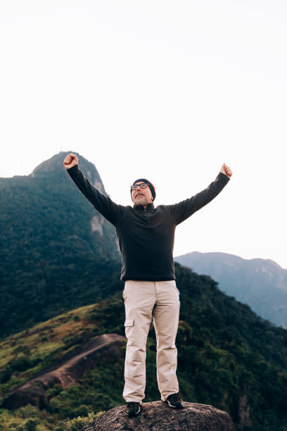 Senior man with arms raised cheering outdoors at the mountain