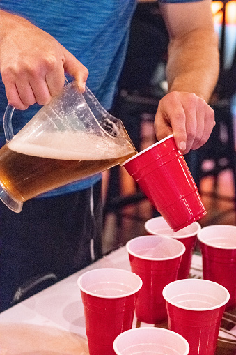 Boy pouring beer from pitcher into red cup at fraternity party