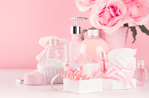 Elegant decor for romantic girlish dressing table - different bath and spa cosmetics, accessories, roses bouquet in pastel pink color on white wood board, closeup.