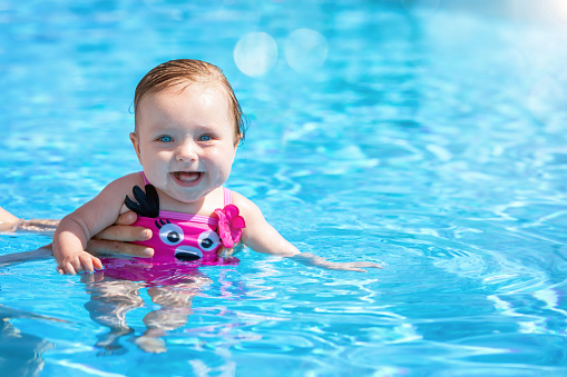Happy, cute baby girl enjoys a hot summer day in the blue waters of a swimming pool