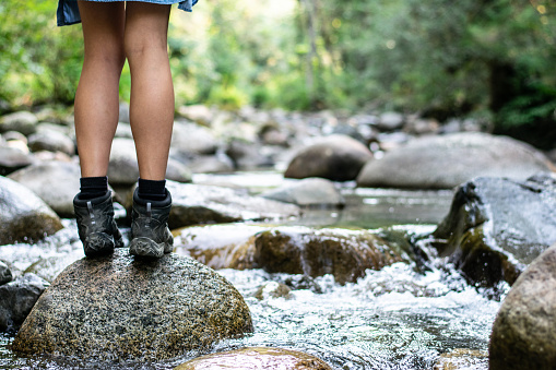Girl in hiking boots standing on rock in river