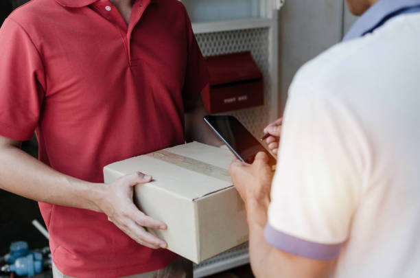 young man customer appending signature in digital mobile phone receiving parcel post box from courier with home delivery service man smiling face in red uniform at home, express delivery concept joven cliente cliente añadiendo firma en el teléfono móvil digital recepción de la casilla de correos de servicio de mensajería con el servicio de entrega a domicilio hombre cara sonriente en uniforme rojo en casa, concepto de entrega exprés