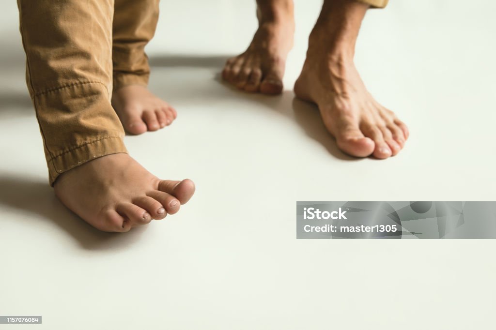 Family's legs on white studio background, dad and son Family's legs on white studio background. Barefoot dad and son standing together. Concept father's day and support, childhood, parenthood, family and relationship. Togetherness and happiness. Father's Day Stock Photo