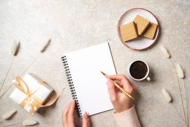 istock Modern minimal home workspace desk with human hand writing text message on blank paper notebook, waffles, dry flowers on concrete stone background. Flat lay style, top view fashion lifestyle blog hero 1157076454