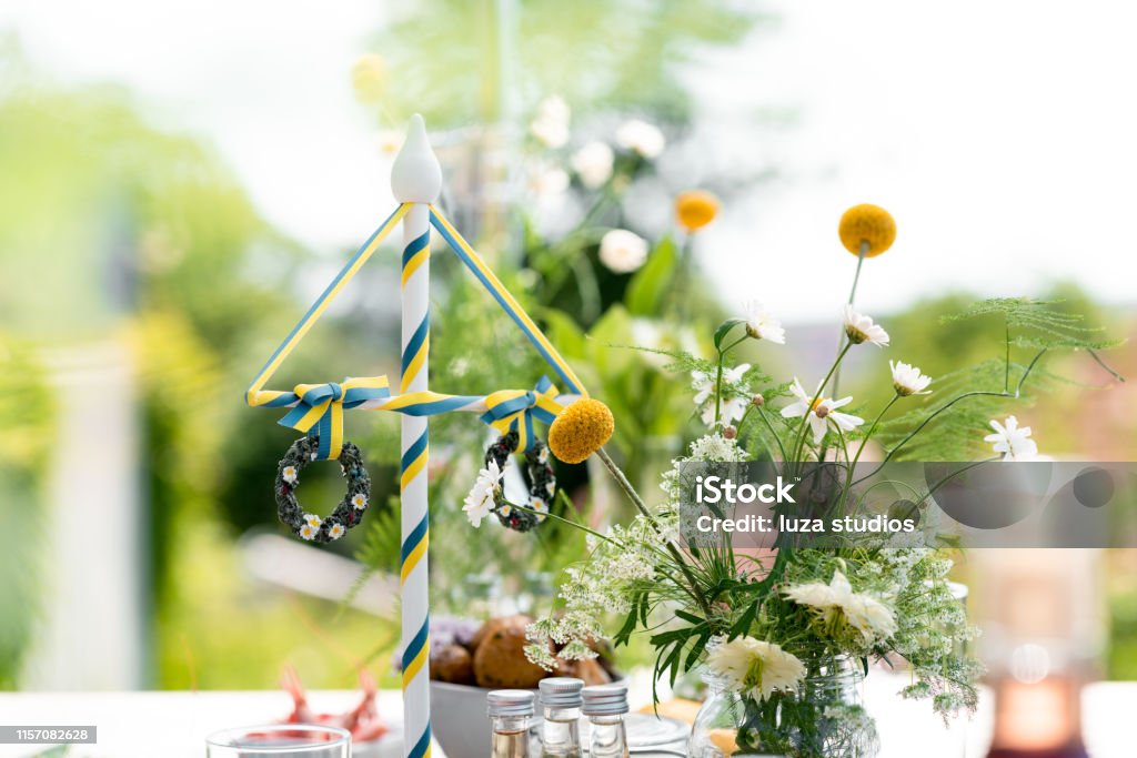 Swedish Midsummer dinner celebrations Traditional Swedish midsummer dinner on. a wooden table out in the sun. Celebrating the summer solstice in Scandinavia. Focus on the maypole with Swedish colors. Sweden Stock Photo