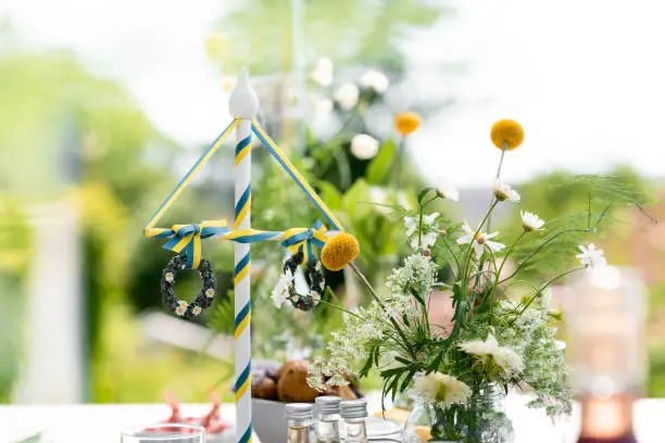 Traditional Swedish midsummer dinner on. a wooden table out in the sun. Celebrating the summer solstice in Scandinavia. Focus on the maypole with Swedish colors.