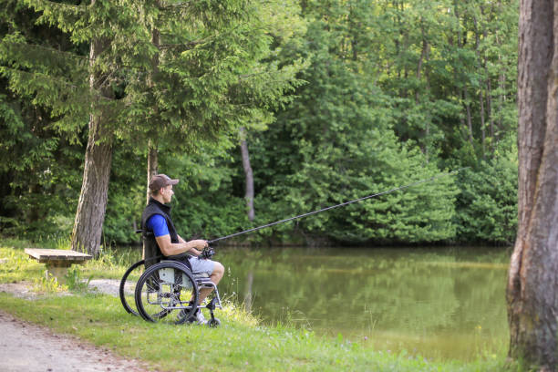 Disabled man on wheelchair fishing in nature Fishing as an accessible competitive sport for people with disabilities and also enjoying in nature for health benefits. paraplegic stock pictures, royalty-free photos & images