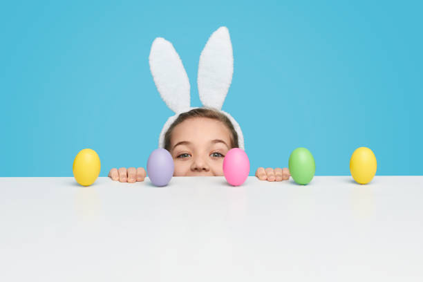 istock Girl with peeking out from behind table with Easter eggs 1157085355