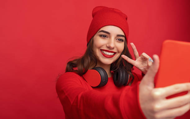 Stylish hipster girl taking selfie on red background