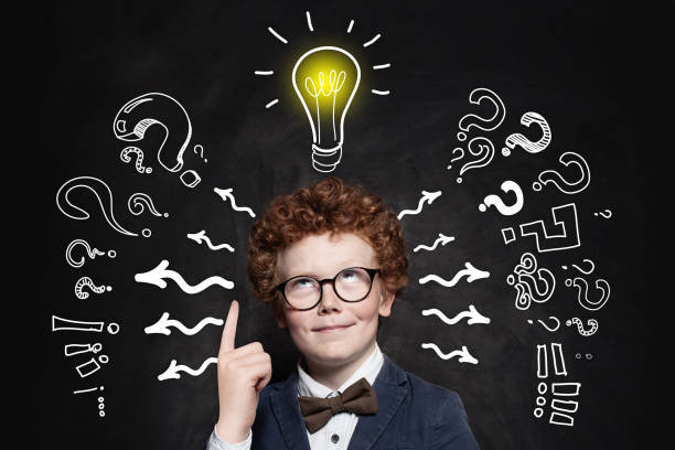 istock Cute boy student pointing up and looking at lightbulb on blackboard background. Idea concept 1157087223