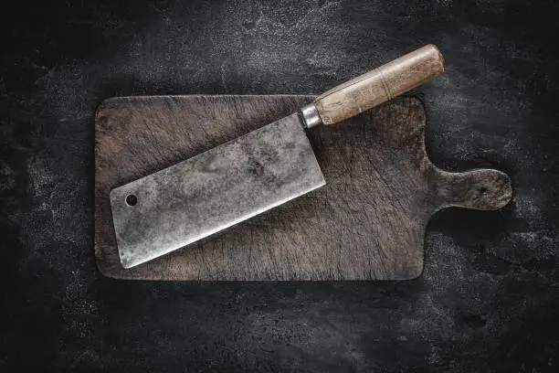Old Butcher Meat Cleaver and Rustic Brown Wood Chopping Board on Dark Background