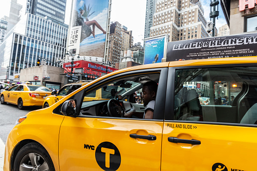 New York City, USA - July 31, 2018: Black driver waiting in a row of taxis on a street with people around and huge advertising screens in Manhattan, New York City, USA