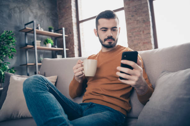 istock Low below angle view portrait of his he nice-looking attractive confident content freelancer bearded guy drinking latte writing sms at industrial loft brick interior style living-room 1157088901