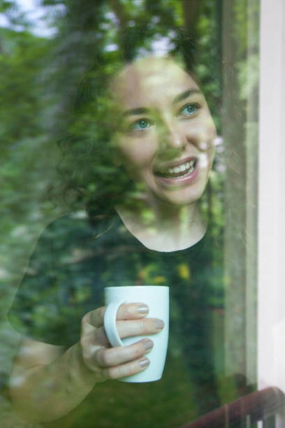 istock Young woman looking out window view through glass 1157090161
