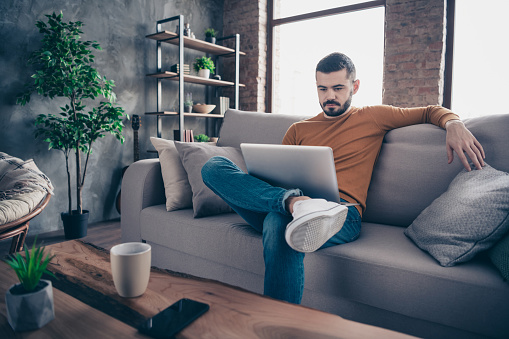 Portrait of focused independent student entrepreneur sit divan domestic look search news creative, smart have solution choice decision dressed denim jeans orange pullover sweater big room