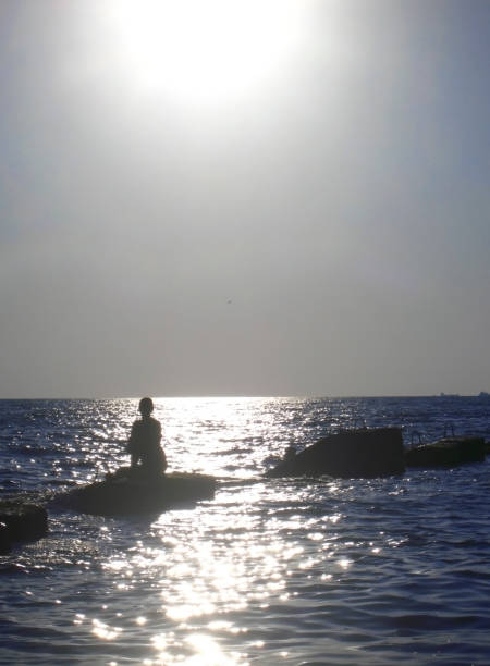 giovane donna sulla pietra sul mare sotto il grande sole - sundow foto e immagini stock