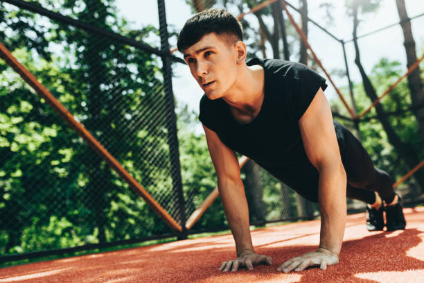 istock Outdoors image of young athletic muscular man doing push-ups on workout ground. Caucasian fitness male doing workout exercises on sunset light background. People and sport concept 1157093341