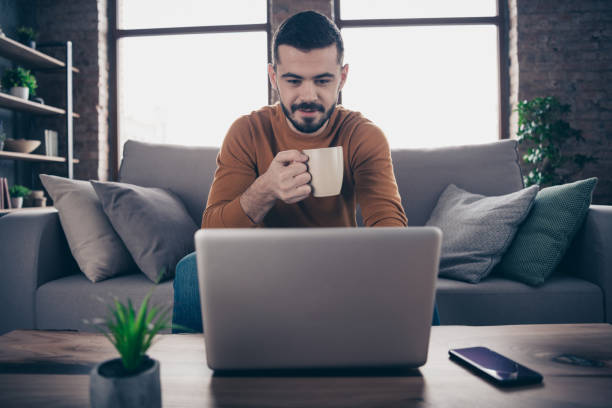 istock Portrait of nice handsome freelancer work worker hold hand beverage mug aroma focused sit divan use user device dressed orange sweater pullover big apartment 1157094636