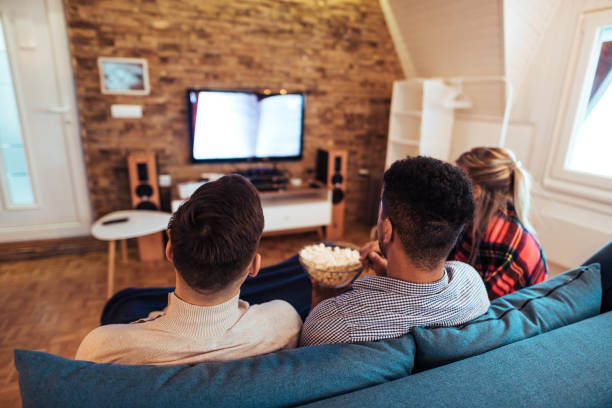 istock Friends watching tv and eating popcorn, rear view. 1157097340