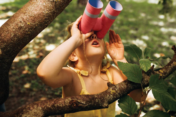 verticale de plan rapproché de petite fille regardant par une jumelles recherchant une imagination ou une exploration dans la journée d'été dans le stationnement. enfant jouant avec le jeu de safari de semblant binoculaire à l'extérieur dans la forê - childs game photos et images de collection