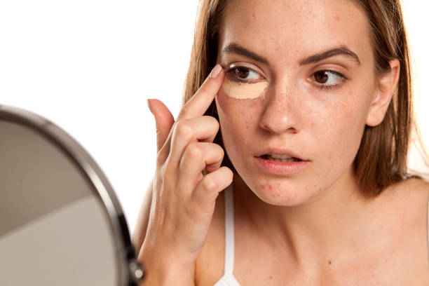 young beautiful girl applying concealer with fingers under her eyes on white backgeound young beautiful girl applying concealer with fingers under her eyes on white backgeound concealer stock pictures, royalty-free photos & images