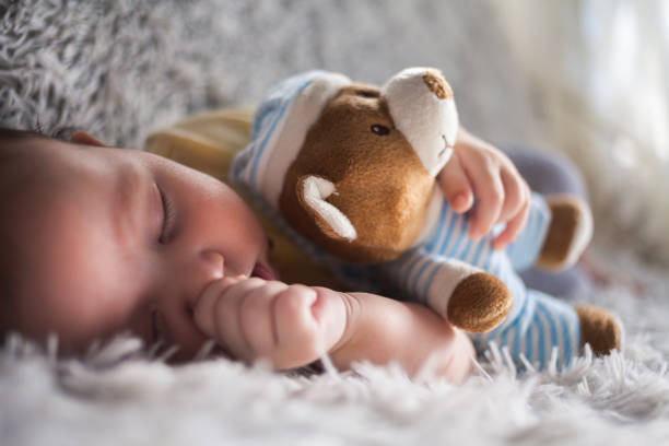 High angle view of a newborn baby lying on a bed with a teddy bear and a nice soft blanket on him.