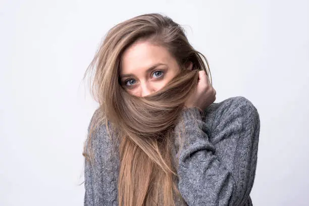 Photo of Portrait of playful young woman holding long hair as scarf hiding and covering