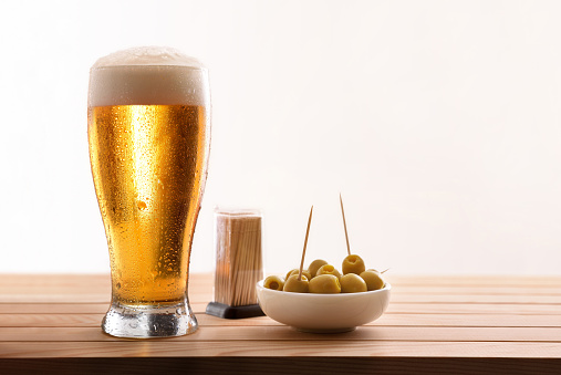 Appetizer with glass of fresh beer on wooden slatted table with white background. Horizontal composition. Front view.