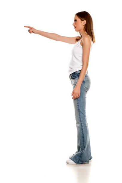 istock Young pretty woman posing in bell bottom jeans on white background, and pointing on empty space 1157099512