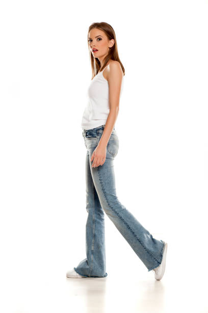 istock Young pretty woman walking in bell bottom jeans on white background 1157099596