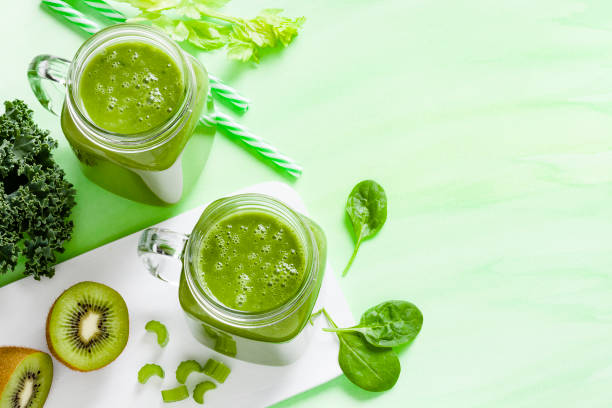High angle view of two glasses filled with green detox drink surrounded by green vegetables shot on green background. The composition is at the left of an horizontal frame leaving a useful copy space for text and/or logo. Predominant color is green. DSRL studio photo taken with Canon EOS 5D Mk II and Canon EF 100mm f/2.8L Macro IS USM.