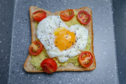 Close up shot avocado toast with a fried egg and cherry tomato
