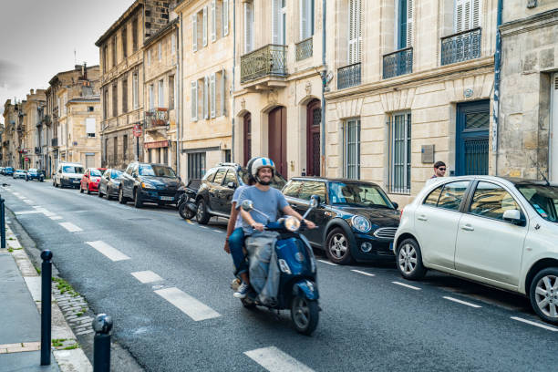Street near the promenade in the centre of Bordeaux, France. In the foreground are a young couple on a moto scooter.