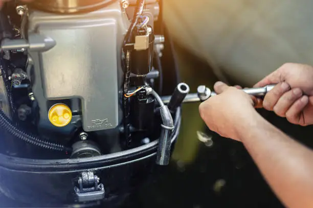 Photo of mechanic repairing inflatable motorboat engine at boat garage. Ship engine seasonal service and maintenance. Vessel motor with open cover