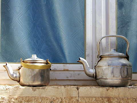 Copper teapots standing to concrete sill, kettles on street shop window before glass. Teapot consisting of copper kettles with handle, spout for draining liquid coffee. Copper kettles is iron teapots.