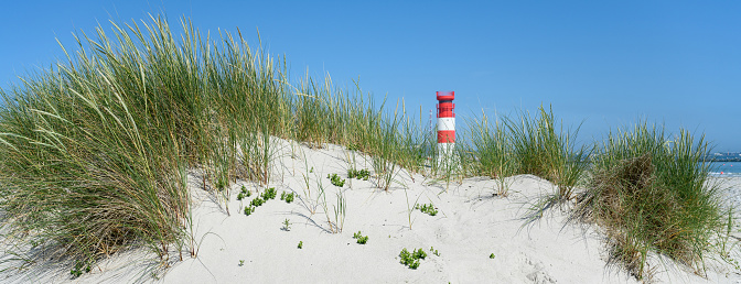 Red and white striped lighthouse on sand dunes at coast of island Helgoland Dune, Germany. Shallow DOF with selective focus on grass in the foreground.