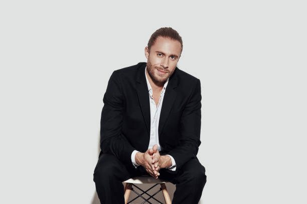 istock Confidence and charisma. Handsome young man in full suit looking at camera while sitting against grey background 1157117313