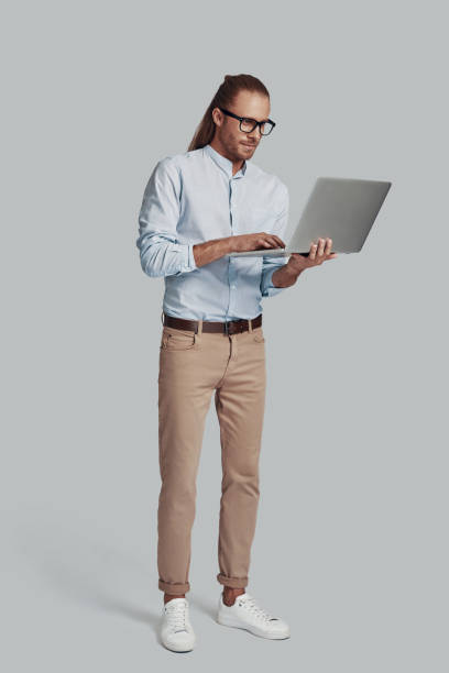 istock Confident business expert. Full length of handsome young man working using laptop while standing against grey background 1157117524