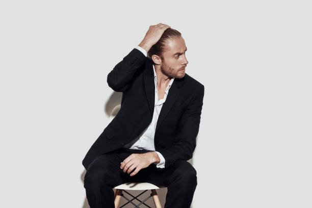 istock Confident in his style. Handsome young man in full suit looking away while sitting against grey background 1157117555