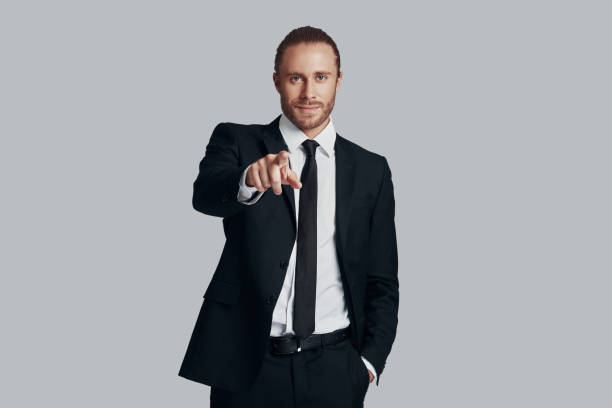 istock I need you! Handsome young man in full suit looking at camera and pointing you while standing against grey background 1157118804