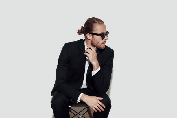 istock Just the way he is. Charming young man in full suit looking away while sitting against grey background 1157118873