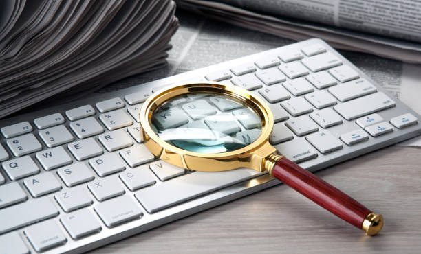 istock magnifier on the keyboard and a stack of newspapers 1157119948