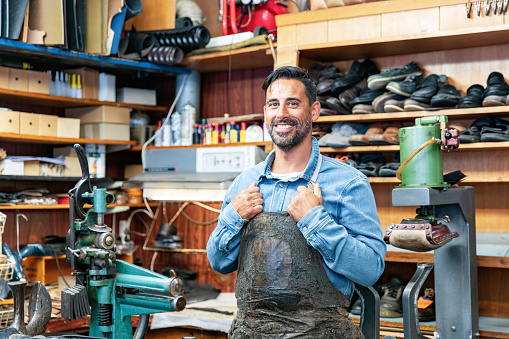 A Latino man is standing in a workshop and is making shoes.