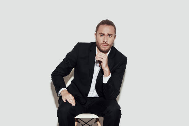 istock Young and confident. Handsome young man in full suit looking at camera while sitting against grey background 1157121609