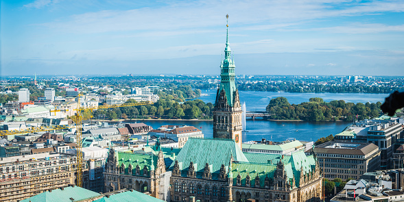 Aerial panorama over the iconic spire of Hamburg Rathaus, Town Hall,  and the fountain rising from the blue waters of the Alster lakes in the heart of Germany’s second city.