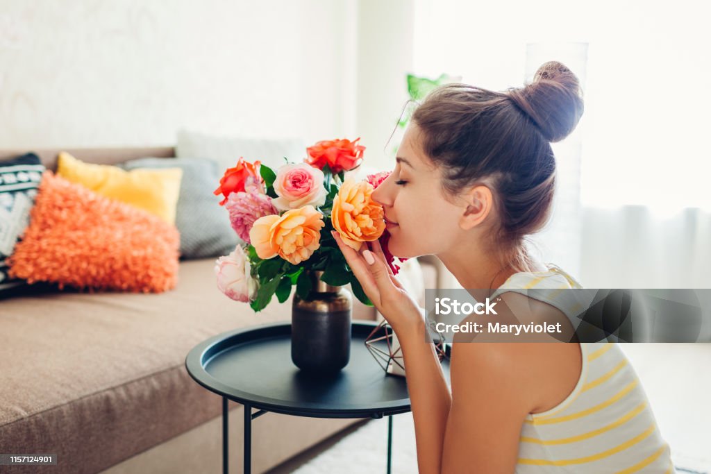 Woman smelling fresh roses in vase on table. Housewife taking care of coziness in apartment. Interior and decor Woman smelling fresh roses in vase on table. Housewife taking care of coziness in apartment. Interior design and decor with flowers Flower Stock Photo