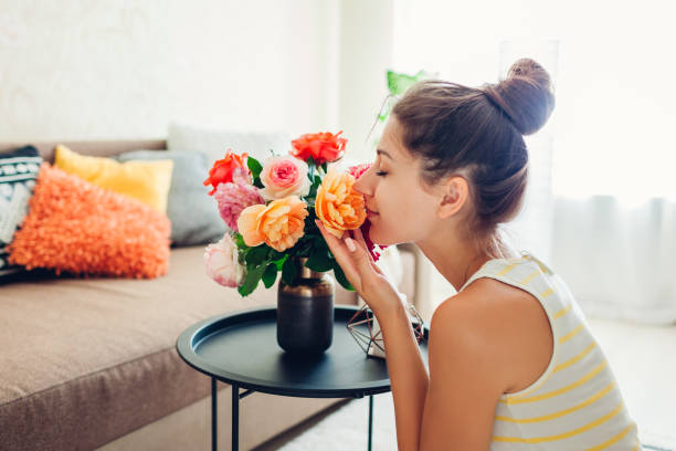 Woman smelling fresh roses in vase on table. Housewife taking care of coziness in apartment. Interior and decor stock photo