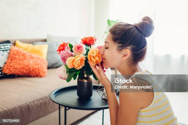 Woman Smelling Fresh Roses In Vase On Table Housewife Taking Care Of Coziness In Apartment Interior And Decor Stock Photo - Download Image Now